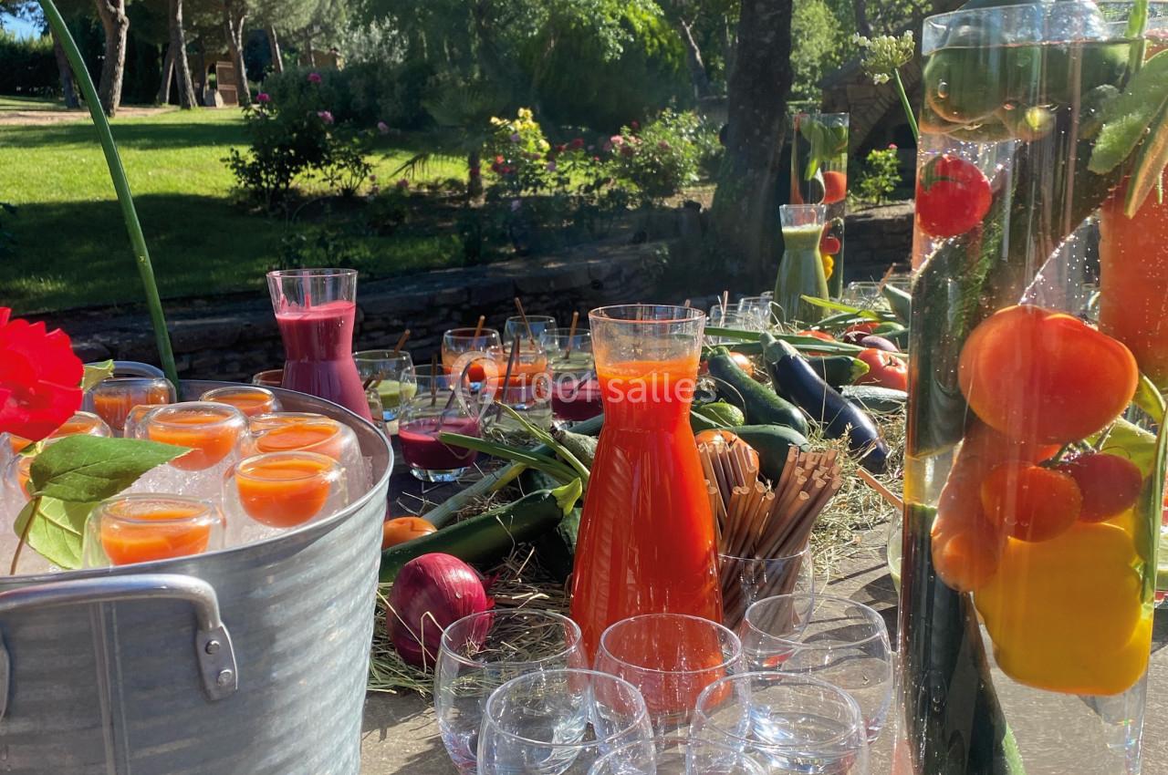 Carafes de jus colorés, légumes et fruits frais disposés sur une table en extérieur, sous un soleil éclatant.