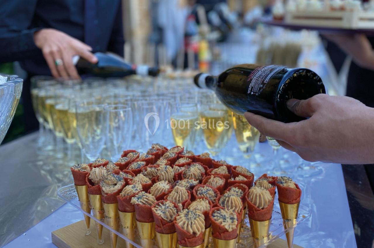Des verrines en forme de cônes garnies, disposées sur un plateau, avec du champagne servi en arrière-plan.
