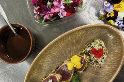 Miniature Traiteur Chaponost (Rhône) - Jacques Lafargue Traiteur #15 Une main coupe un rouleau de foie gras sur une planche en bois, entouré de figues et de tomates cerises.