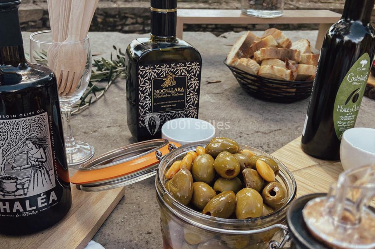 Bocaux d'olives, bouteilles d'huile d'olive et pain disposés sur une table en extérieur.