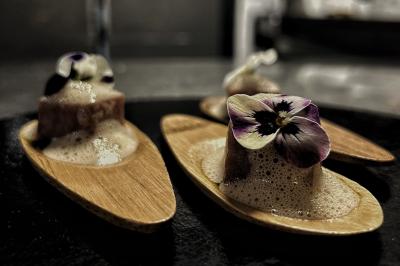 Miniature Traiteur Chaponost (Rhône) - Jacques Lafargue Traiteur #31 Une main coupe un rouleau de foie gras sur une planche en bois, entouré de figues et de tomates cerises.