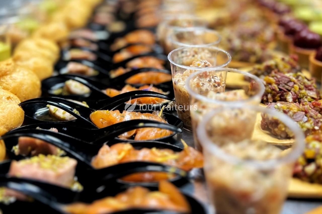 Assortiment de bouchées apéritives variées disposées sur une table, comprenant verrines, poissons et autres mets.