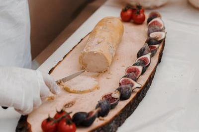 Miniature Traiteur Chaponost (Rhône) - Jacques Lafargue Traiteur #36 Une main coupe un rouleau de foie gras sur une planche en bois, entouré de figues et de tomates cerises.