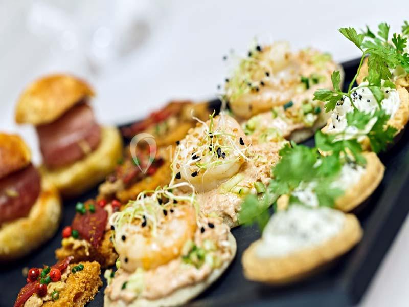 Plateau de bouchées apéritives variées, comprenant des canapés garnis de crevettes, herbes fraîches et autres ingrédients.