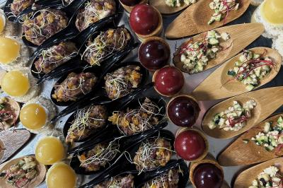 Une main coupe un rouleau de foie gras sur une planche en bois, entouré de figues et de tomates cerises.