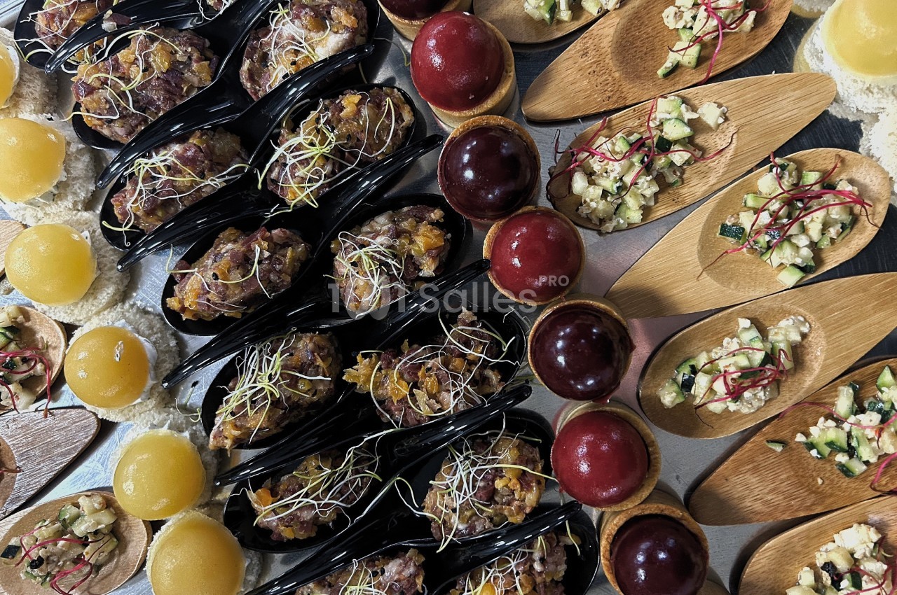 Assortiment de bouchées apéritives variées, incluant tartares, billes colorées et préparations sur cuillères en bois.
