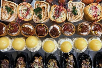 Une main coupe un rouleau de foie gras sur une planche en bois, entouré de figues et de tomates cerises.