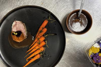 Une main coupe un rouleau de foie gras sur une planche en bois, entouré de figues et de tomates cerises.