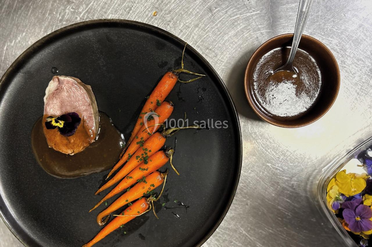 Assiette gastronomique avec magret de canard, carottes glacées, sauce et fleurs comestibles, accompagnée d'une coupelle de…
