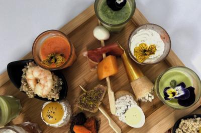 Une main coupe un rouleau de foie gras sur une planche en bois, entouré de figues et de tomates cerises.