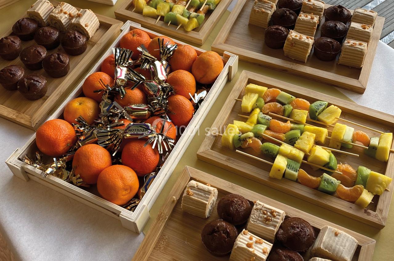 Plateaux en bois contenant des fruits frais, des pâtisseries et des friandises, disposés sur une table blanche.