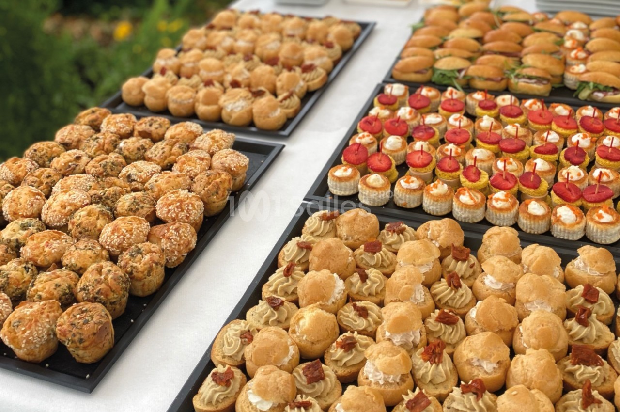 Plateaux de petits fours variés disposés sur une table blanche lors d'un buffet en extérieur.
