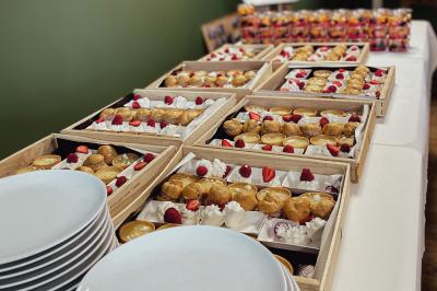 Une main coupe un rouleau de foie gras sur une planche en bois, entouré de figues et de tomates cerises.