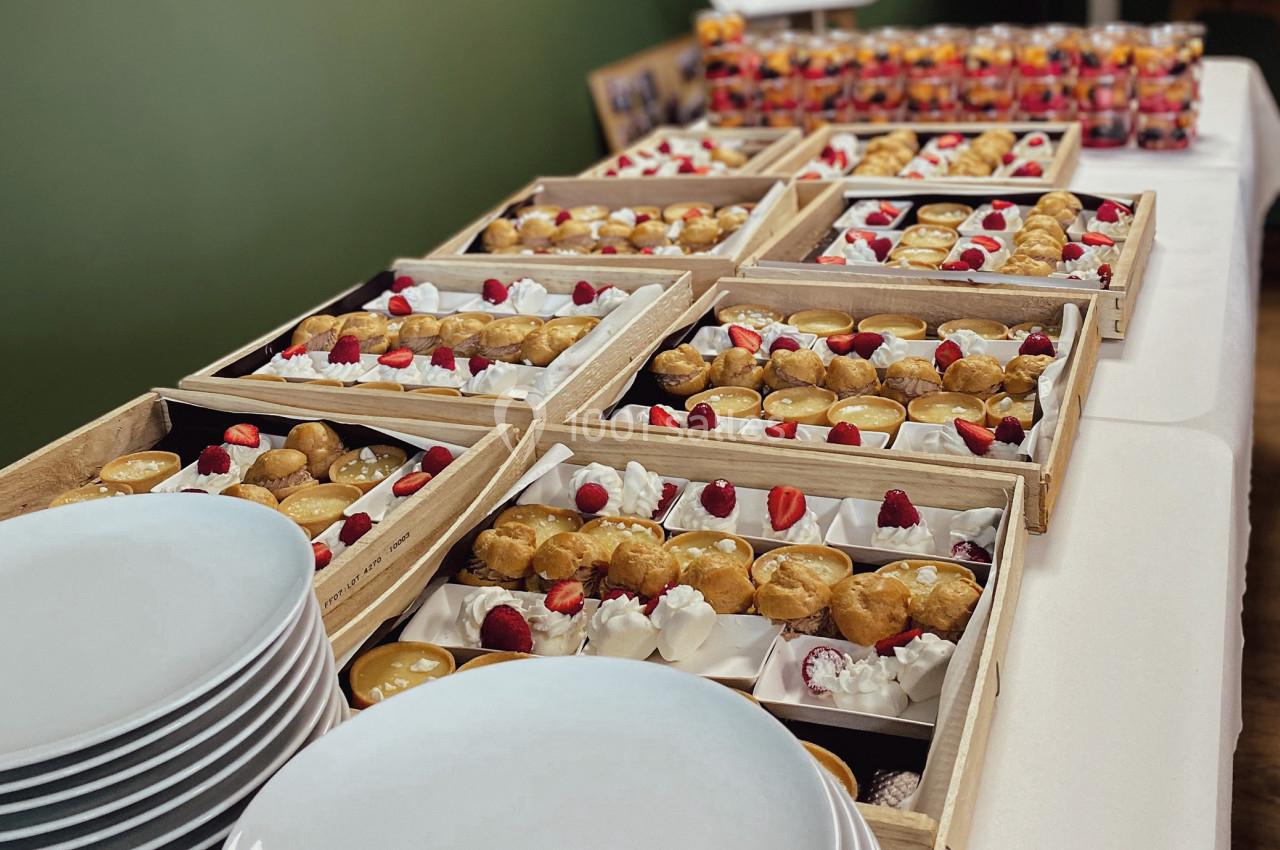 Plateaux de desserts variés avec fruits rouges et crèmes, disposés sur une table près d'assiettes empilées.