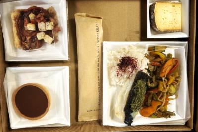 Une main coupe un rouleau de foie gras sur une planche en bois, entouré de figues et de tomates cerises.