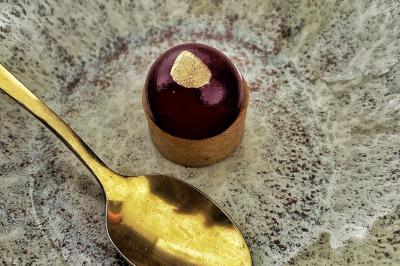 Une main coupe un rouleau de foie gras sur une planche en bois, entouré de figues et de tomates cerises.