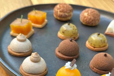 Miniature Traiteur Neuilly-sur-Seine (Hauts-de-Seine) - Arômes et Sens #10 Assortiment de mini-pâtisseries variées sur une assiette noire, disposées sur une table en bois.