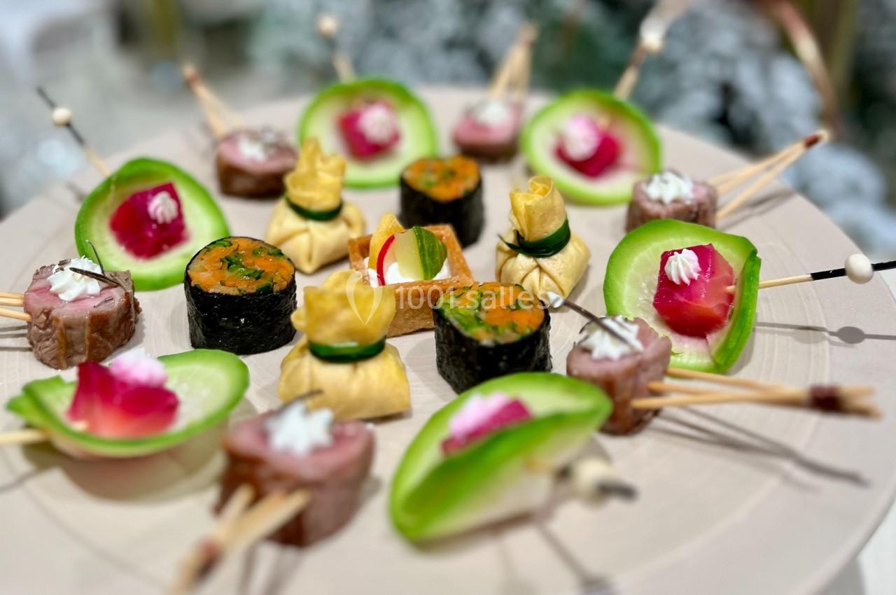 Assortiment de bouchées apéritives variées, incluant sushis, roulés de viande et légumes, présentées sur un plateau.