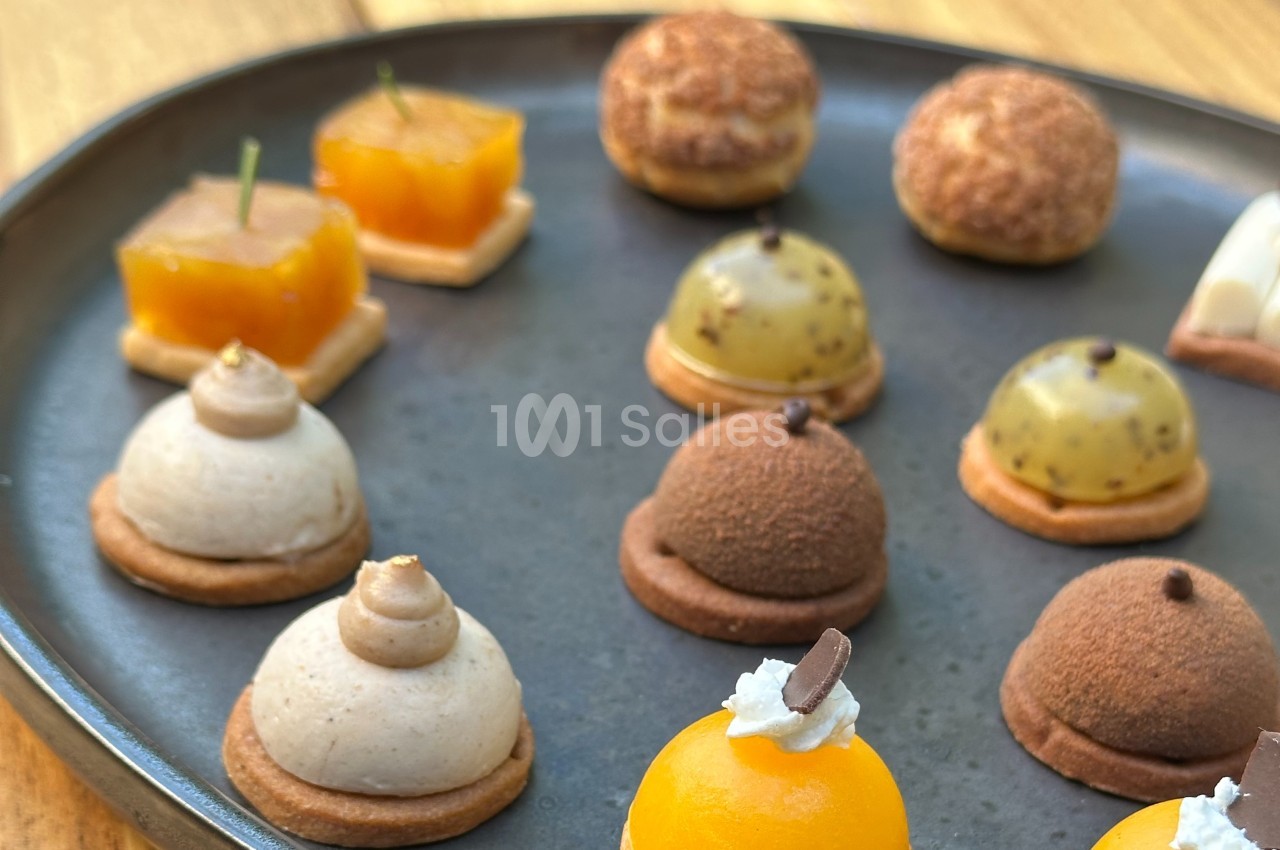 Assortiment de mini-pâtisseries variées disposées sur une assiette noire, présentées sur une table en bois.