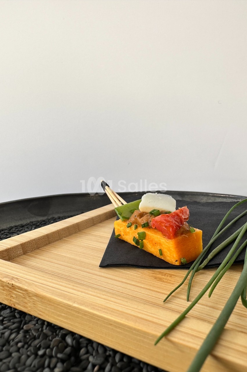 Bouchée de polenta garnie de tomate confite, fromage et ciboulette, présentée sur un plateau en bois avec décoration…