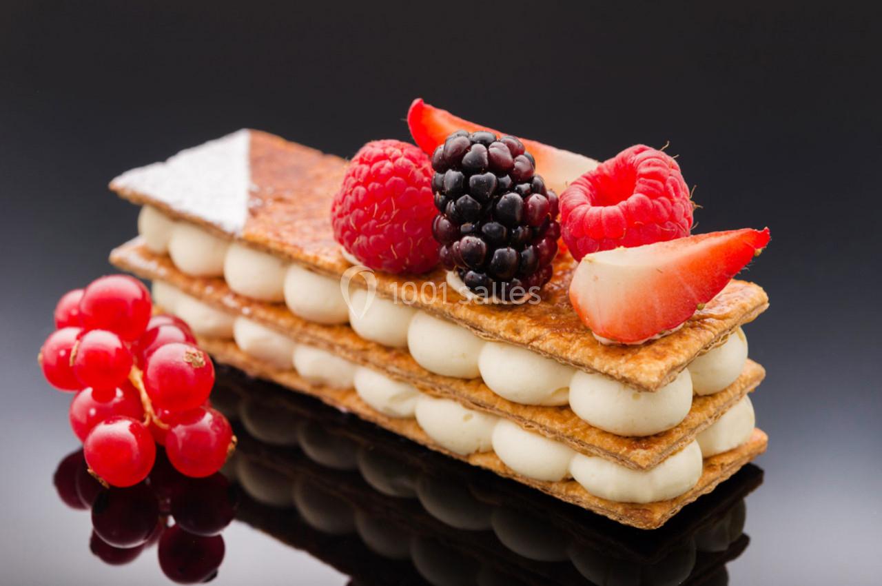 Millefeuille garni de crème vanillée, décoré de framboises, mûres, fraises et groseilles sur fond noir.