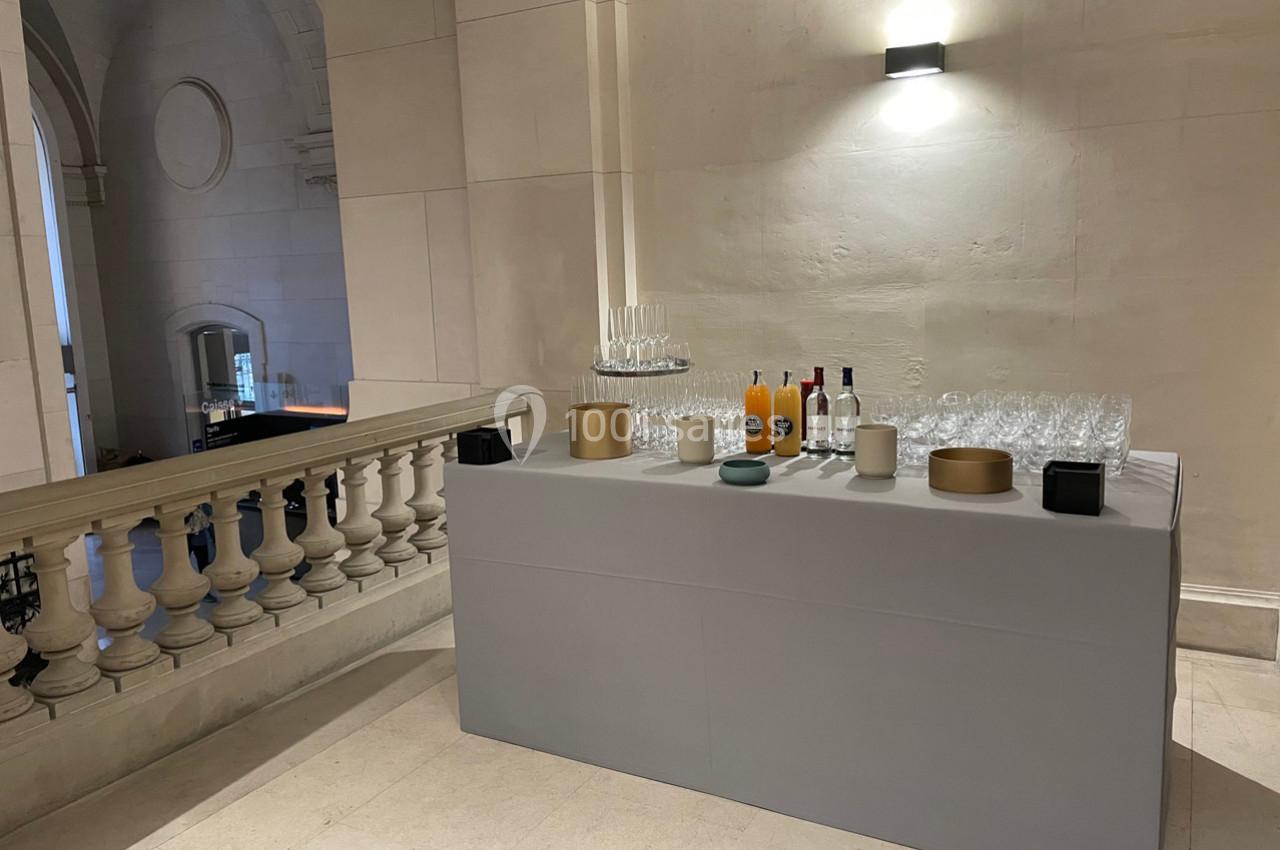 Table avec boissons, verres et carafes disposée dans un espace intérieur lumineux avec balustrade en arrière-plan.