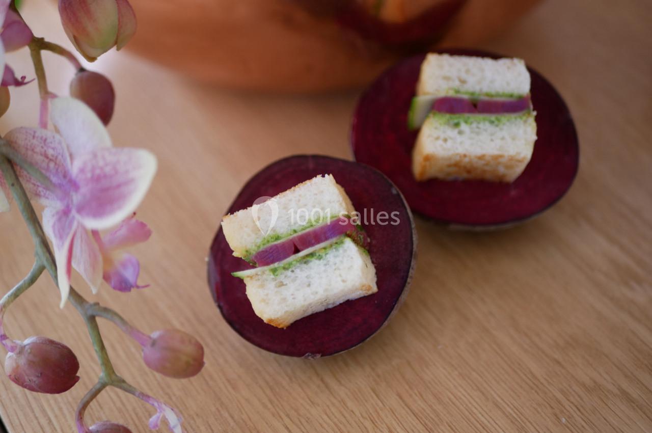 Deux mini-sandwichs garnis de légumes verts et d'oignons rouges, posés sur des tranches de betterave, avec une orchidée en…