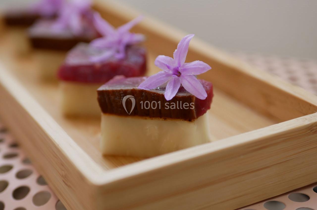 Assortiment de bouchées gastronomiques décorées de fleurs violettes, présentées dans un plateau en bois.