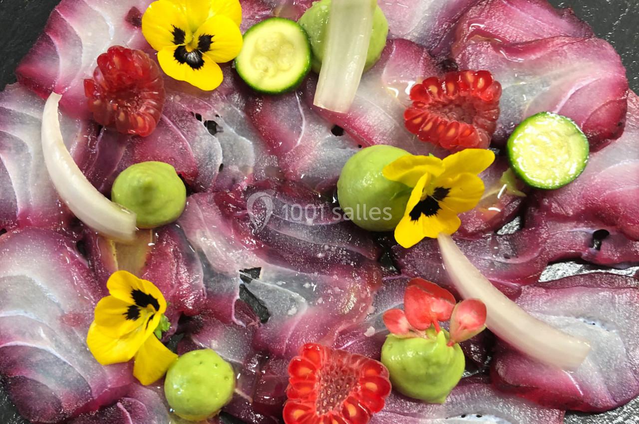 Carpaccio de poisson cru décoré de fleurs comestibles, framboises, courgettes, oignons marinés et purée verte.