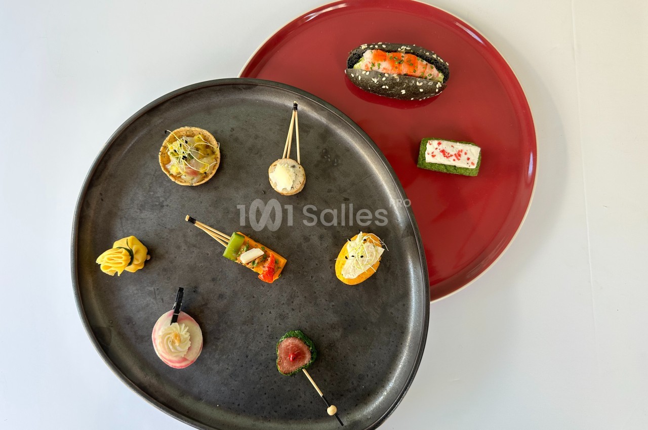 Assortiment de bouchées apéritives variées présentées sur des assiettes noire et rouge.