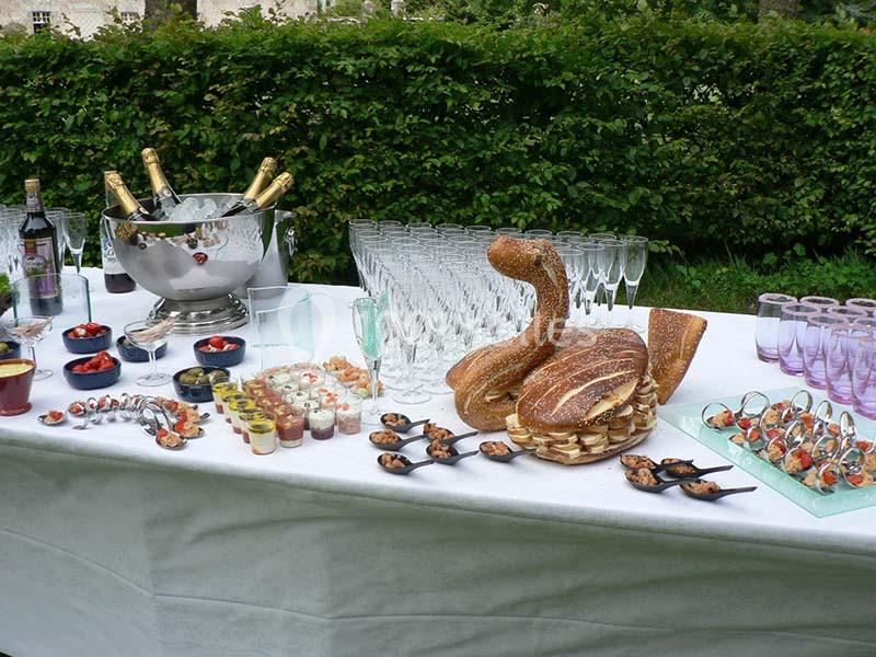 Table dressée avec des verrines, coupes de champagne, bouteilles, et pain en forme de cygne, en extérieur.
