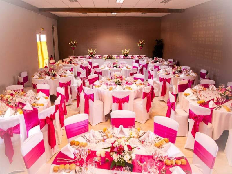 Salle de réception décorée avec des nappes blanches et des nœuds roses, tables dressées pour un banquet.