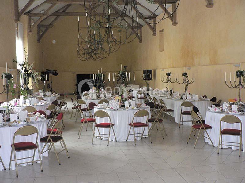 Salle de réception décorée avec des tables rondes dressées, des chaises pliantes et des chandeliers élégants.