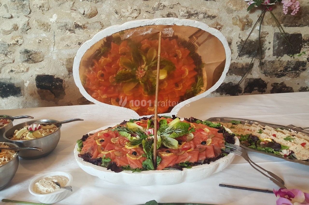 Plateau de saumon fumé disposé en forme de coquillage, entouré de salades et accompagnements sur une table dressée.