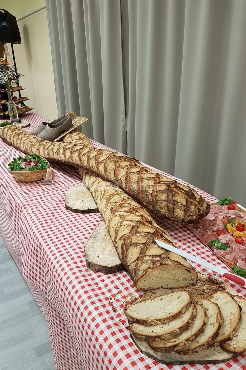 Deux longues baguettes artisanales sur une table à nappe rouge et blanche, entourées de charcuterie et de pain tranché.