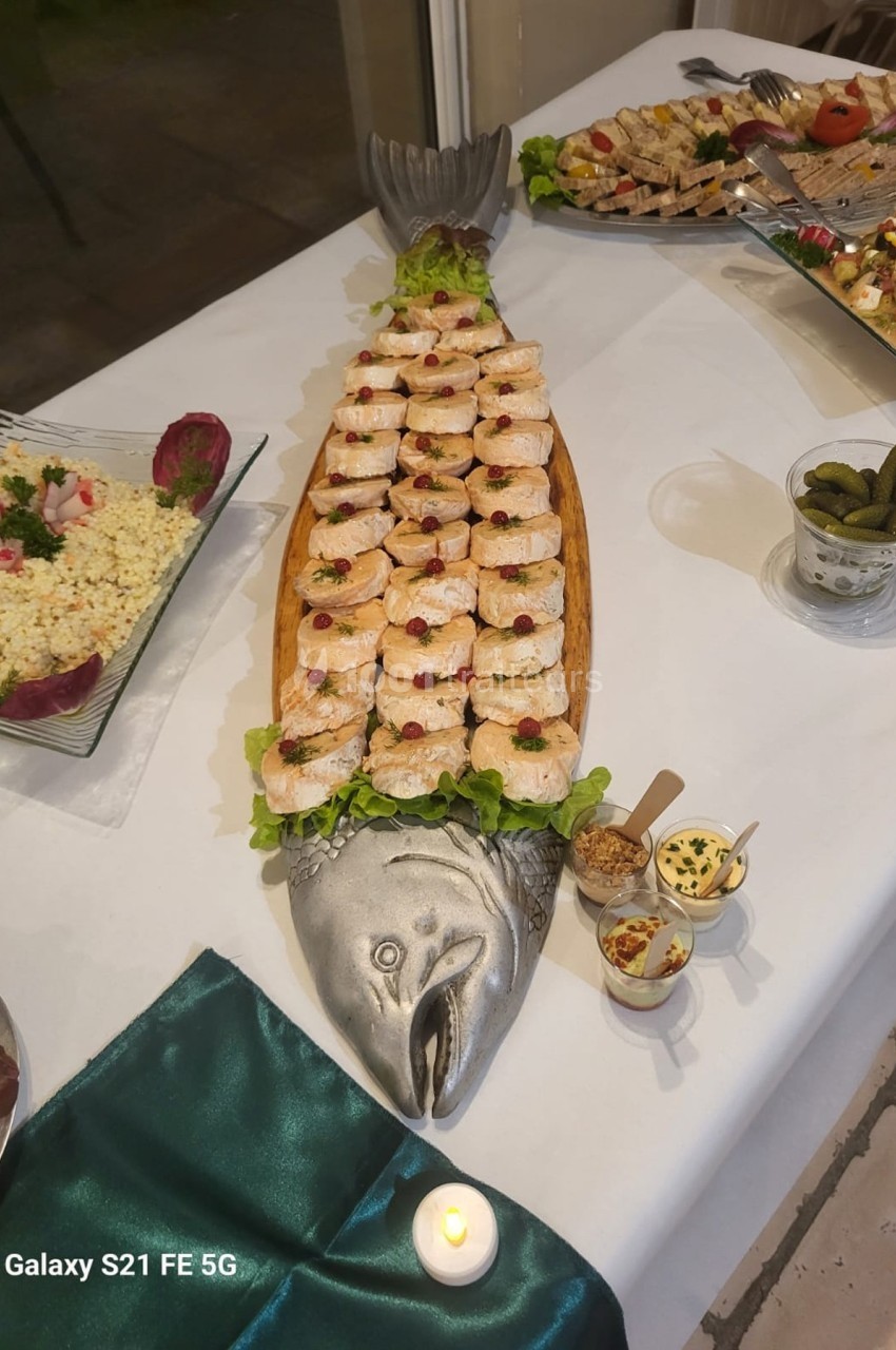 Présentation de bouchées de saumon sur un grand plat en forme de poisson, entouré de divers accompagnements.