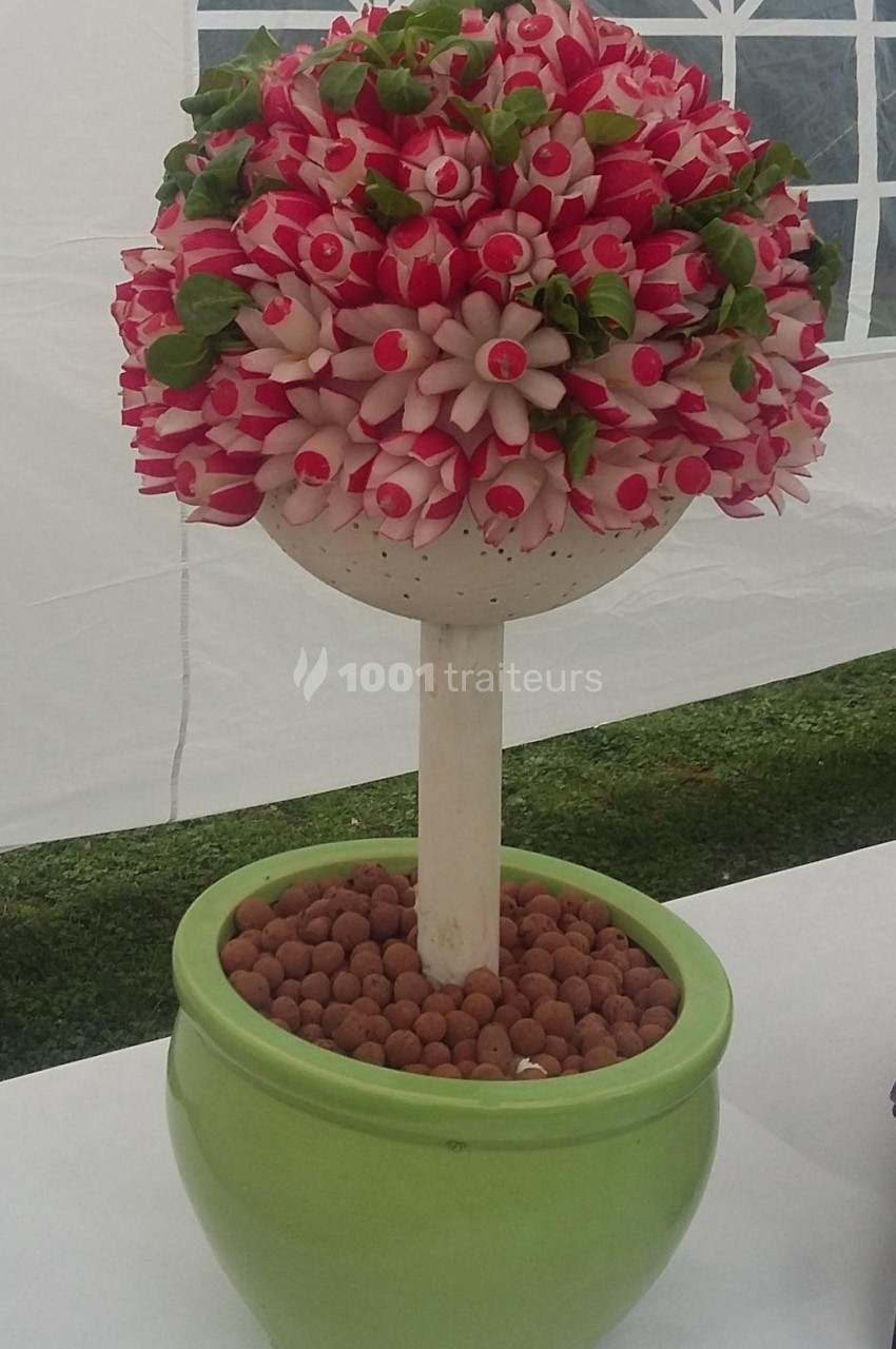 Composition décorative en forme d'arbre réalisée avec des radis rouges et blancs dans un pot vert rempli de billes d'argile.