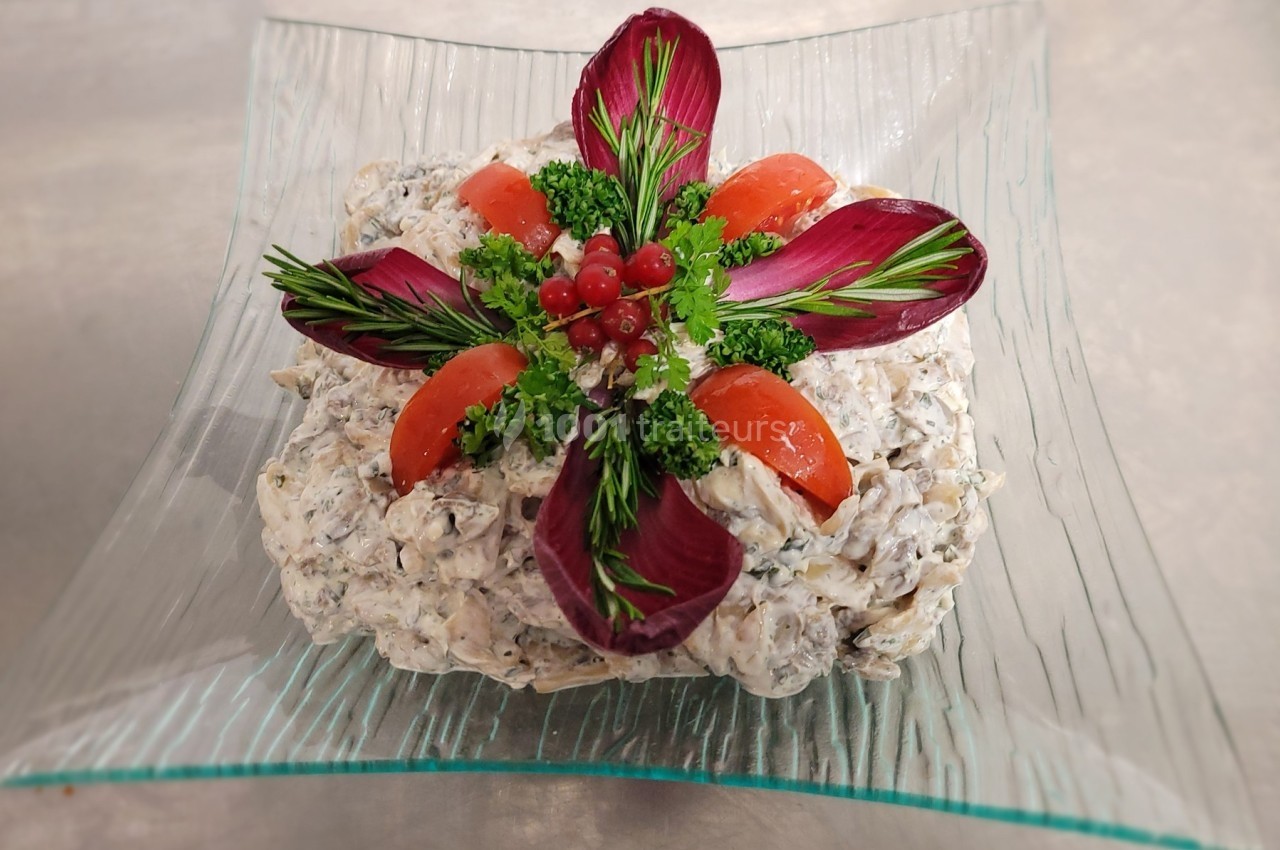 Salade crémeuse garnie de tomates, feuilles de radicchio, persil, romarin et groseilles rouges sur une assiette en verre.