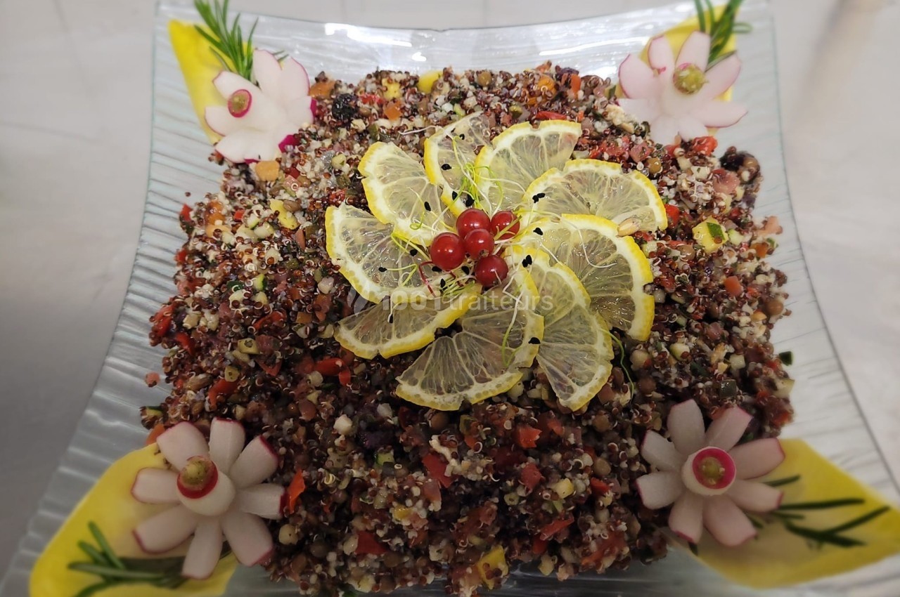 Salade de quinoa colorée garnie de tranches de citron, groseilles rouges et décorations de légumes sur un plat carré.