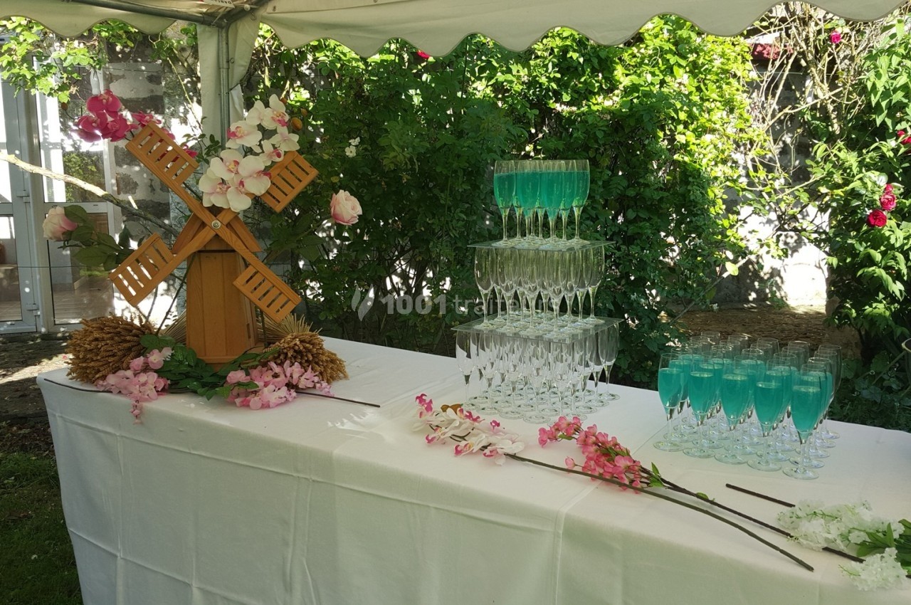 Table décorée pour une réception en extérieur avec verres empilés, cocktails bleus et décorations florales.