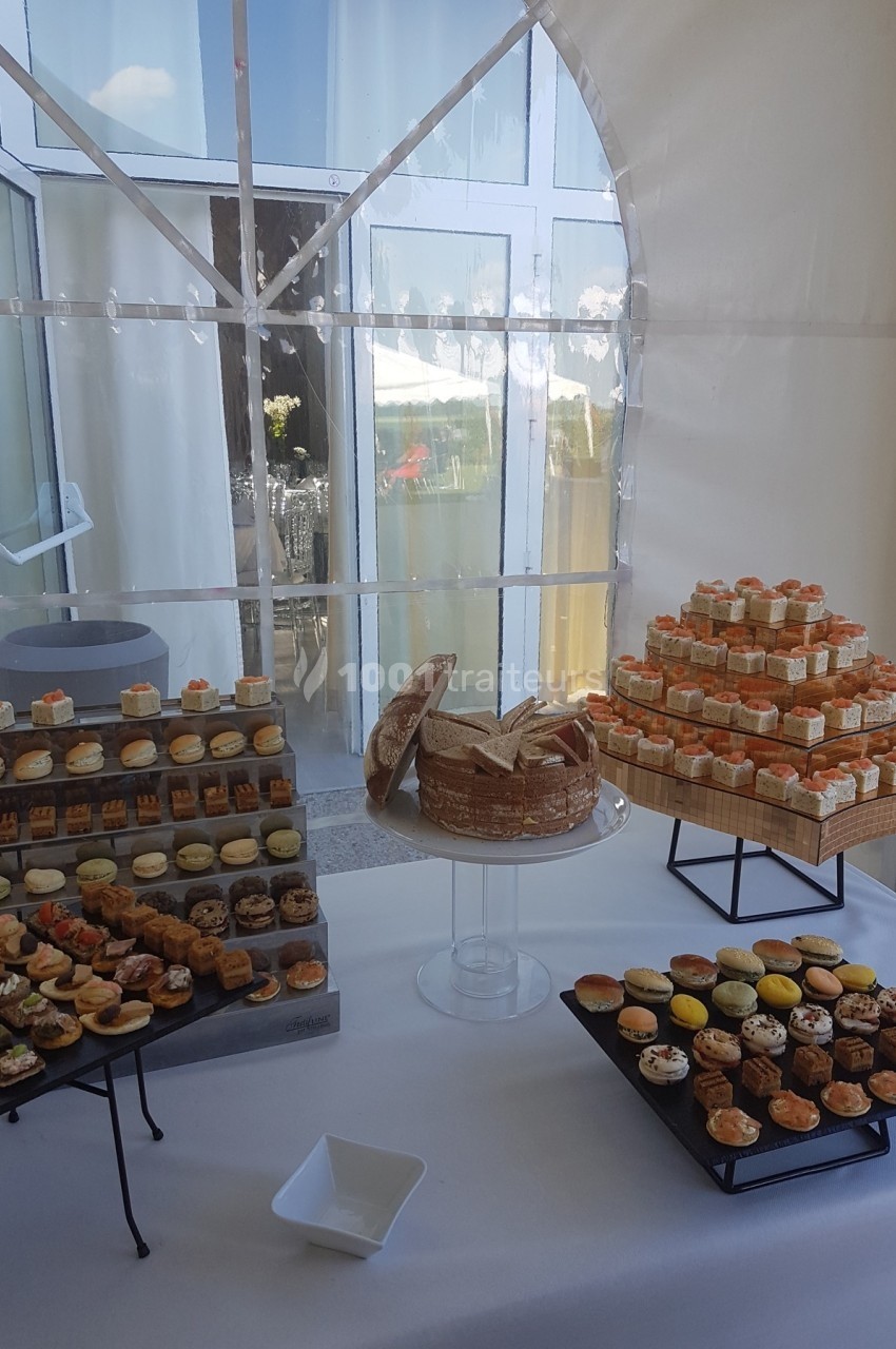 Buffet de petits fours variés disposés sur des plateaux et présentés dans une salle lumineuse avec des baies vitrées.