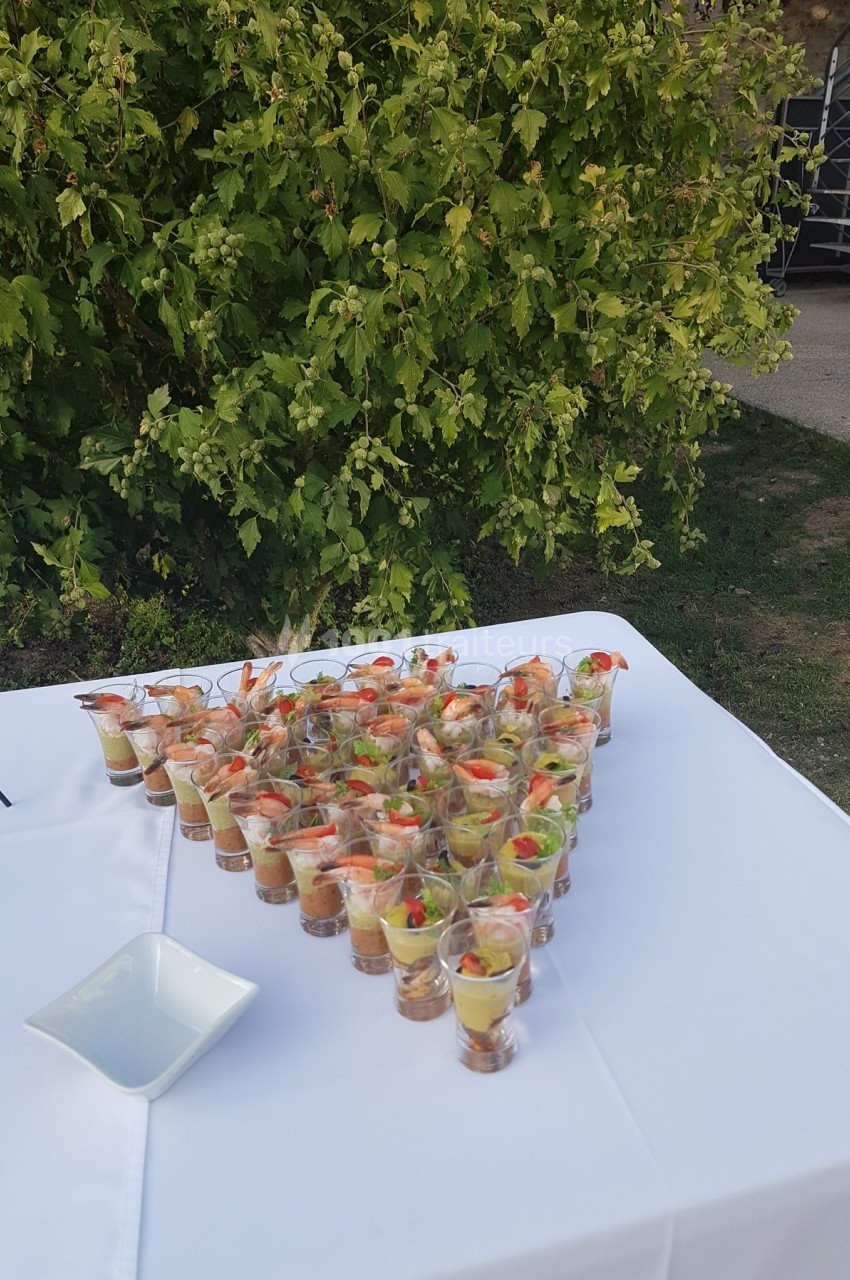Verrines apéritives disposées en triangle sur une nappe blanche, avec un fond de verdure.