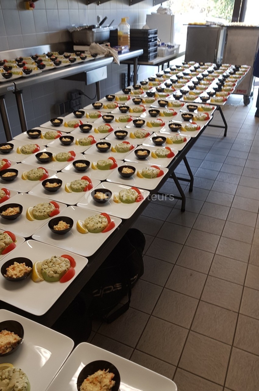 Assiettes dressées avec des entrées variées alignées sur plusieurs tables dans une cuisine professionnelle.