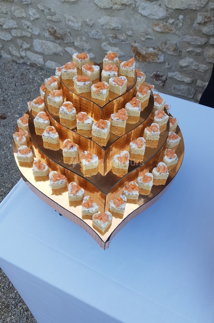 Plateau en forme de cœur avec des bouchées apéritives au saumon disposées sur plusieurs niveaux.