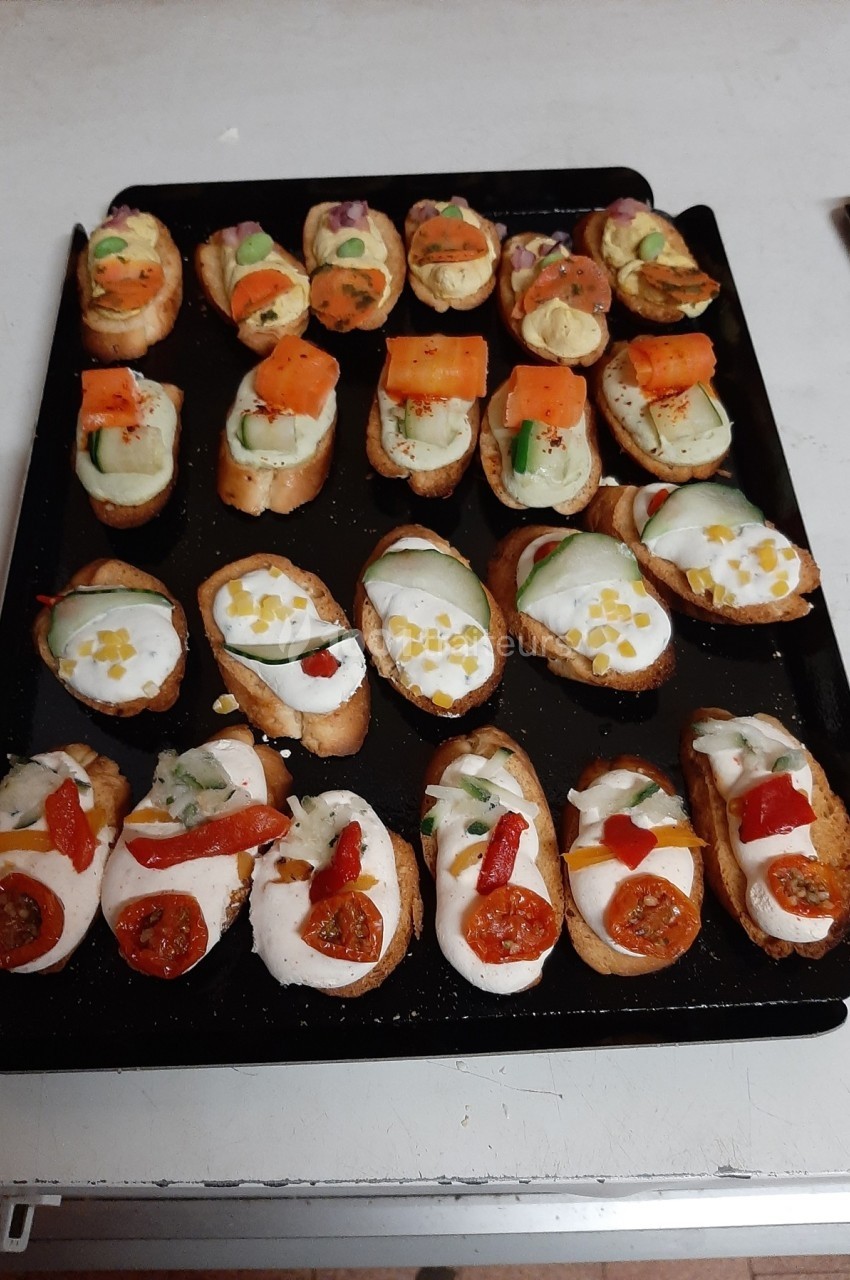 Plateau de toasts variés garnis de légumes, fromage et herbes, disposés sur une plaque noire.