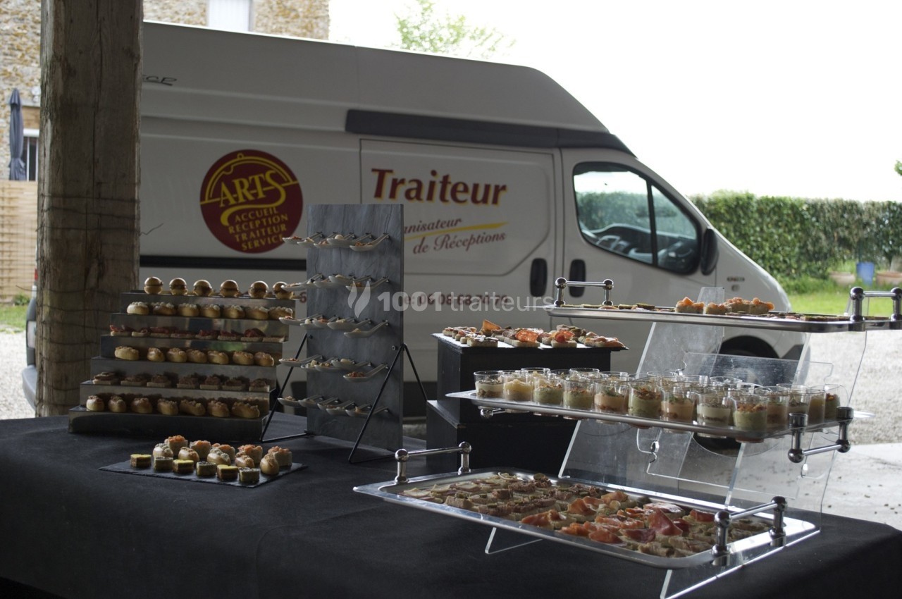 Buffet de verrines et amuse-bouches disposé sur des présentoirs, avec un camion de traiteur en arrière-plan.
