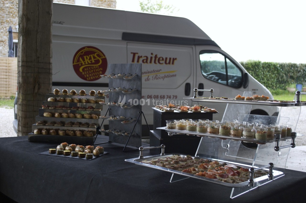 Buffet de verrines et amuse-bouches disposé sur des présentoirs devant un camion de traiteur stationné.