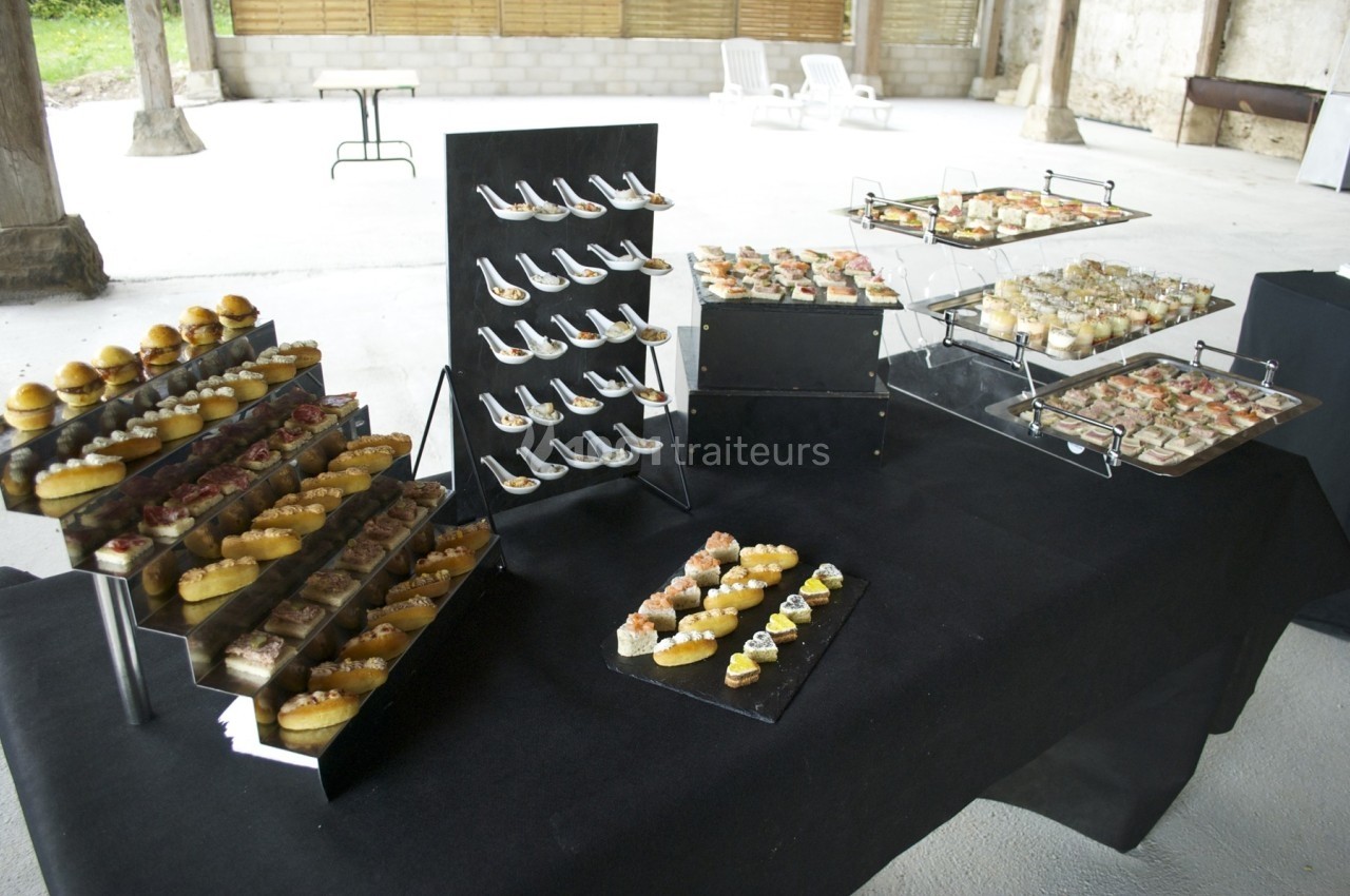 Buffet de bouchées apéritives variées disposées sur des présentoirs noirs dans un espace ouvert et lumineux.