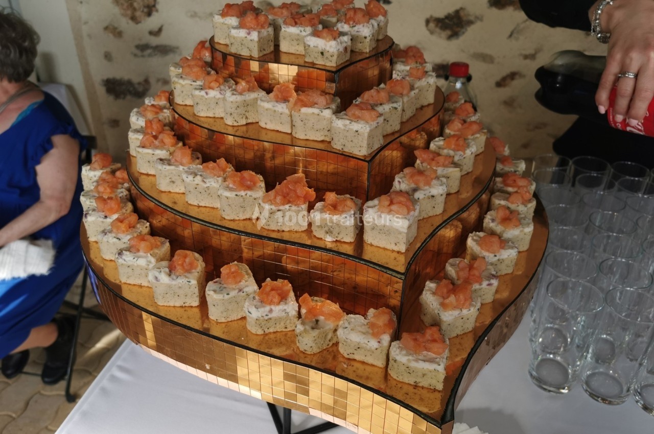Plateau de petits amuse-bouches disposés en pyramide, garnis de mousse et de saumon, sur une table de réception.
