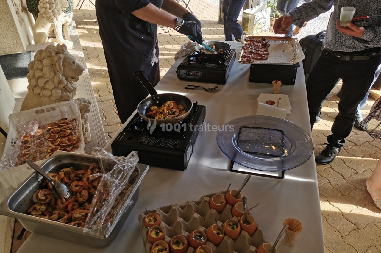 Chef cuisinant des plats à base de fruits de mer et d'œufs devant une table dressée en extérieur.